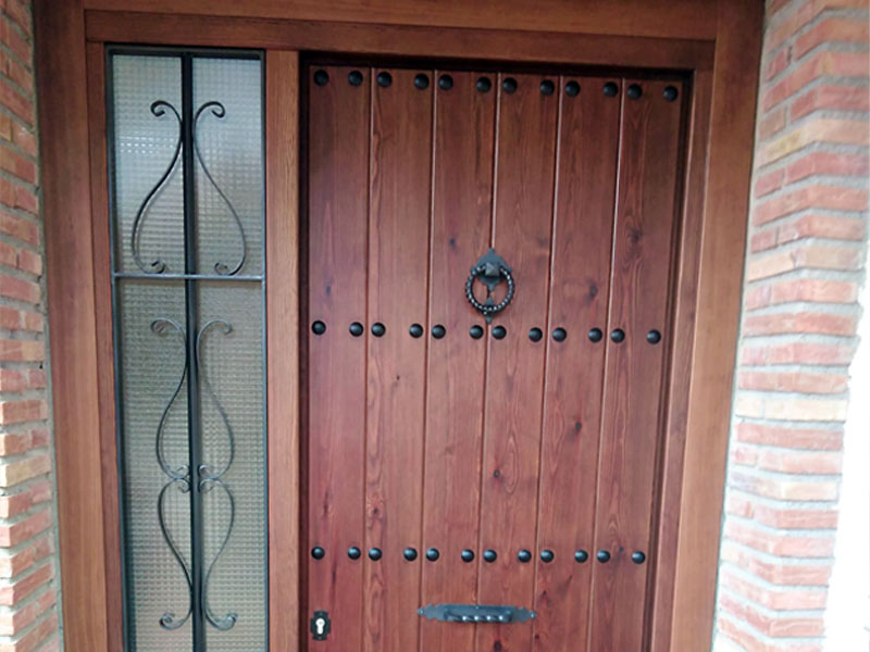 Puerta para exterior fabricada con duelas en madera de nogal y forja